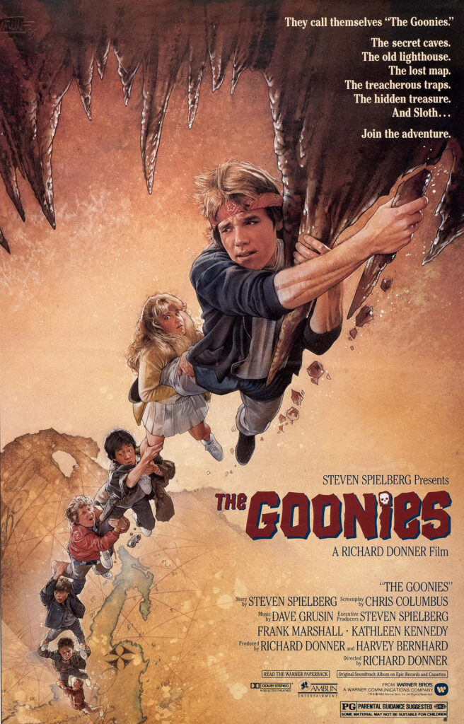 Poster for The Goonies showing a group of kids hanging onto each other in a chain, suspended from a rocky cave ceiling. Text describes their adventure involving secret caves, treasure maps, traps, and hidden treasure. The title "The Goonies" appears in bold red lettering at the bottom.