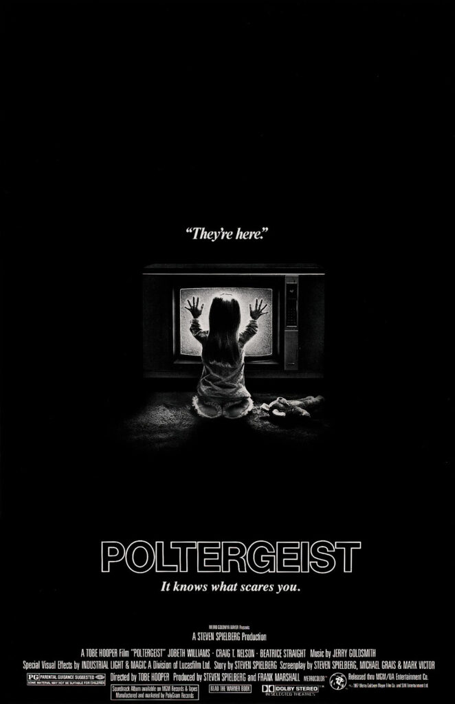 Black-and-white movie poster for Poltergeist showing a young child kneeling in front of a glowing television with both hands pressed against the screen. Above the image are the words, “They’re here.”